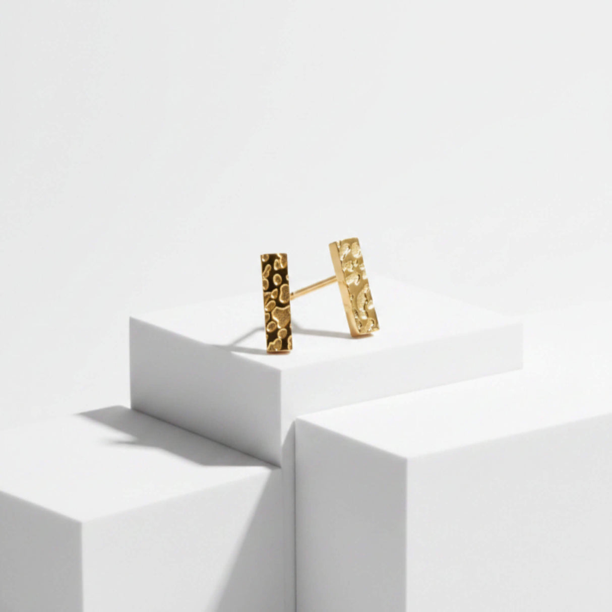 Gold bar stud earrings on plinth