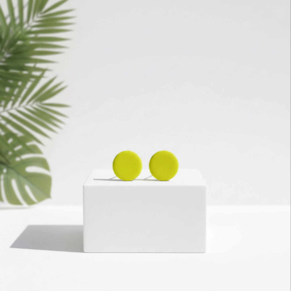 small lemon yellow stud earrings, handmade clay jewellery at lottie of london, lifestyle image on plinth